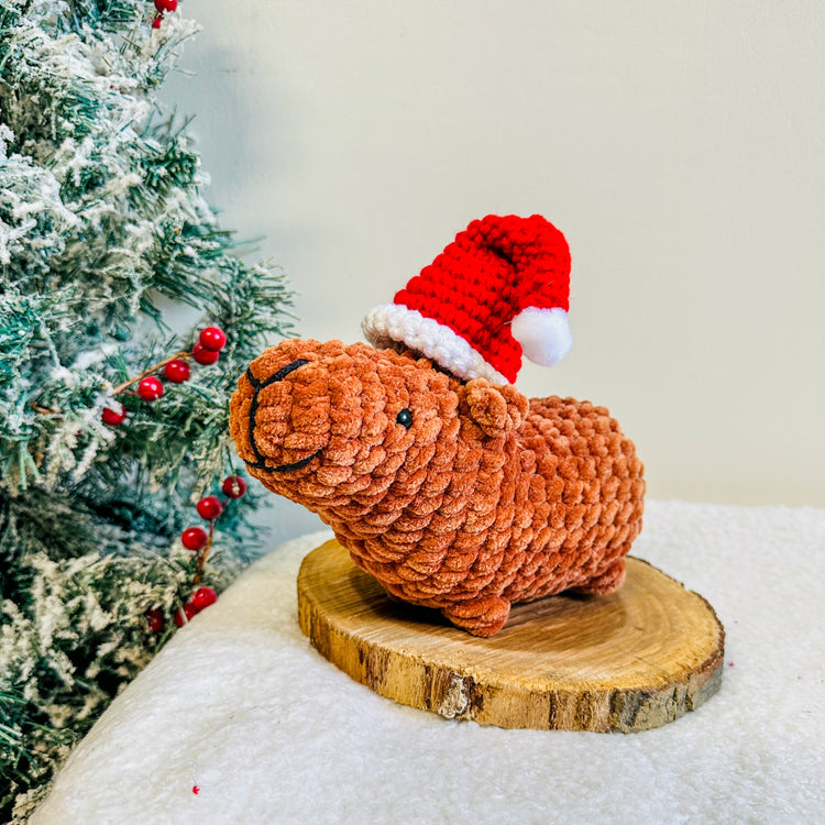 capyabra wearing a christmas hat next to a christmas tree