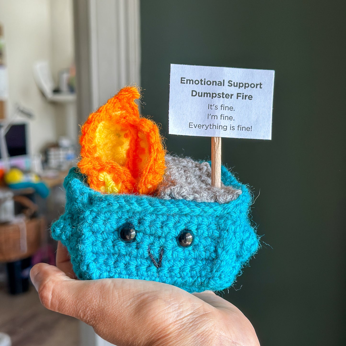 Amigurumi dumpster fire gift with sign that says “It’s fine. I’m fine. Everything is fine.”