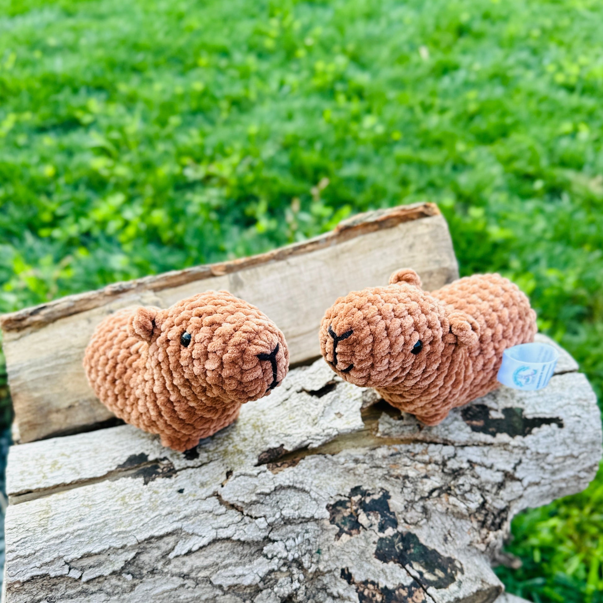 two crochet capybaras standing on a log