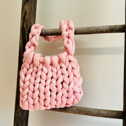 Hand knit chunky pink bag hanging on a ladder