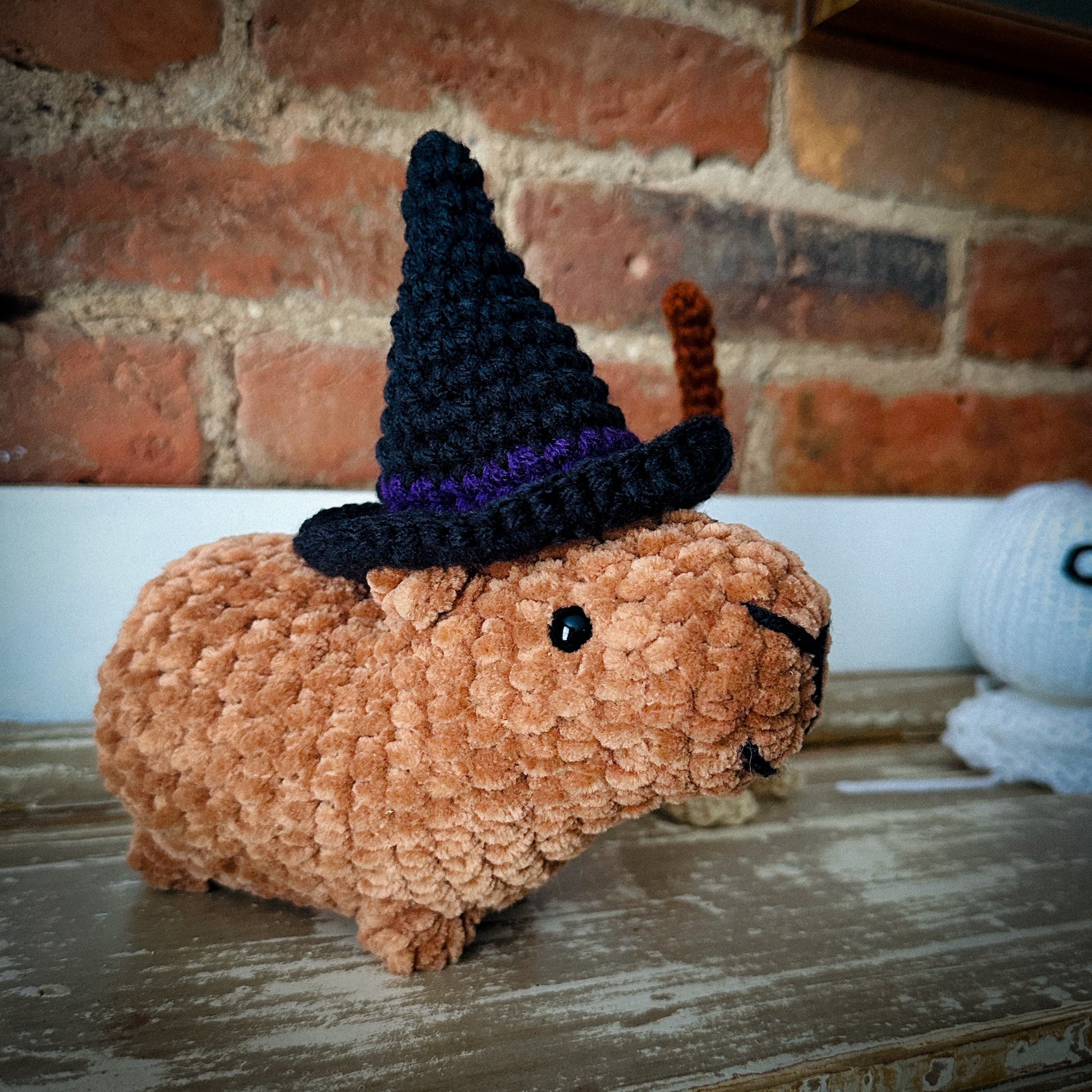 crochet capybara wearing a black and purple witch hat