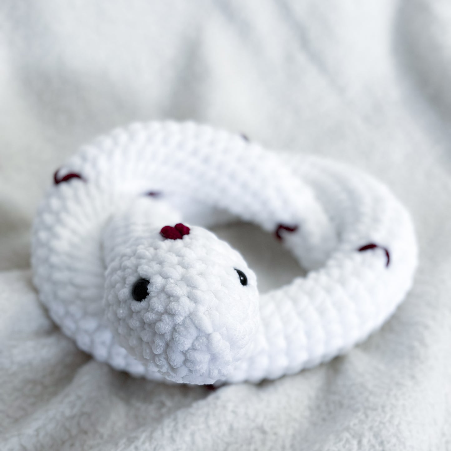 White plush snake toy with red spots on a soft gray background