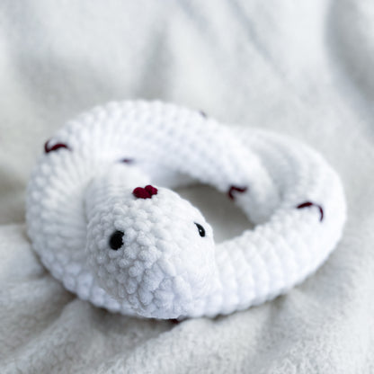 White plush snake toy with red spots on a soft gray background